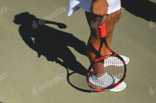 Preview: Low section of female african american player standing with tennis racket at court on sunny day