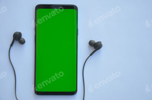 Preview: High angle shot of smartphone phone with green screen and black color earphone