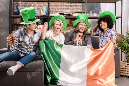 Preview: happy multicultural friends watching tv on saint patrick day with irish flag