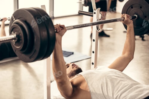 Preview: handsome sportsman lifting barbell with heavy weight plates in gym
