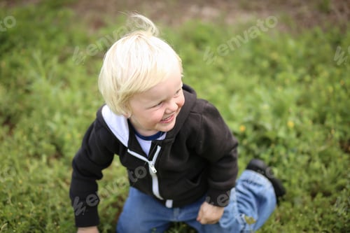 Preview: Happy adorable blonde Australian kid standing on his knees on the grass