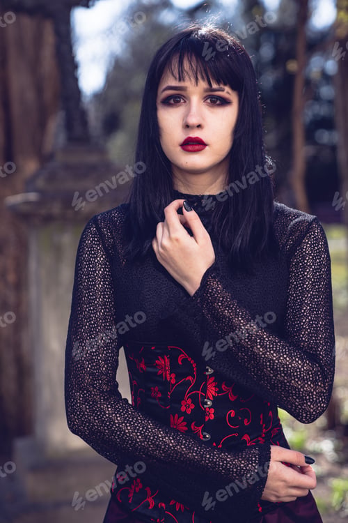 Preview: Pretty gothic caucasian female in a black dress posing in the park, vertical shot