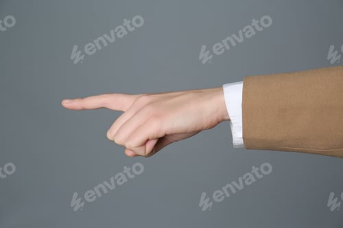 Preview: Businesswoman pointing at something on grey background, closeup. Finger gesture