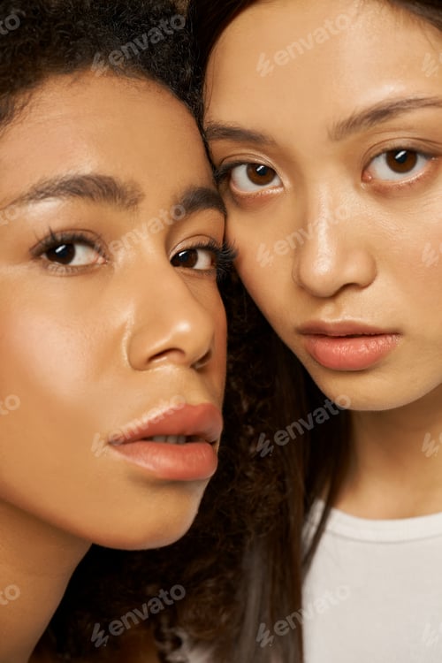 Preview: Face closeup of two beautiful mixed race young women with perfect glowing skin looking at camera