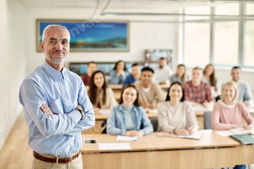 Preview: Happy mature teacher standing with arms crossed in the classroom full of university students.