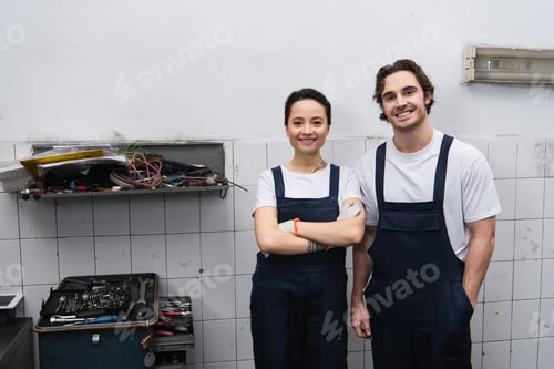 Preview: Smiling mechanics looking at camera near tools in car service