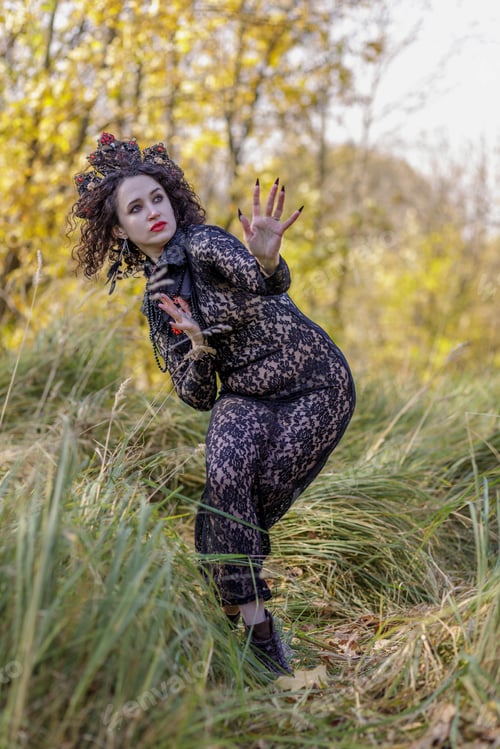 Preview: A woman dressed as a witch stands in an autumn forest. A Gothic queen on Halloween.