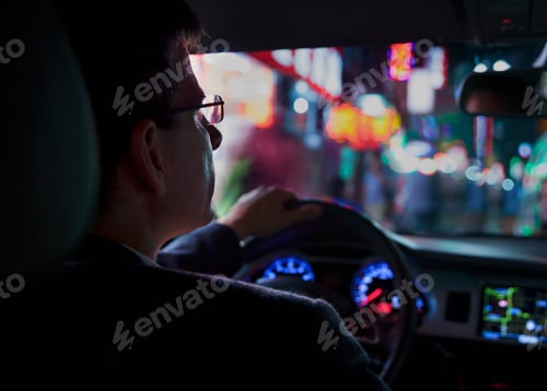 Preview: Over the shoulder view of businessman driving at night in the city, illuminated city lights