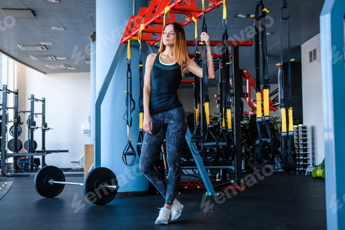 Preview: Joyful girl wearing sportswear holding a suspension fitness straps in the gym