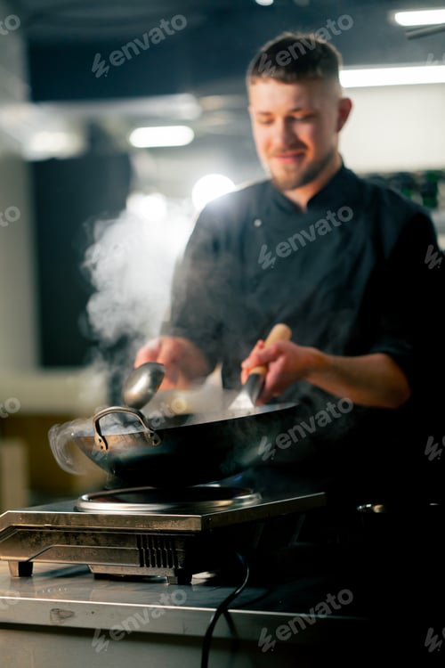 Preview: in professional kitchen the chef prepares wog noodles with vegetables on a large frying pan