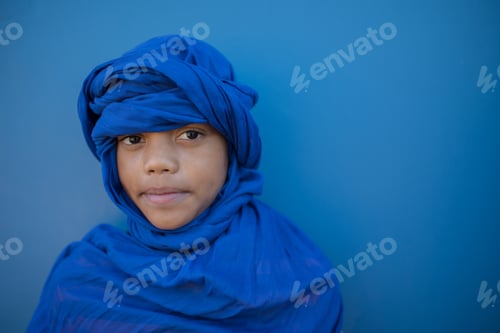 Preview: Close up portrait of boy wearing headscarf against blue background