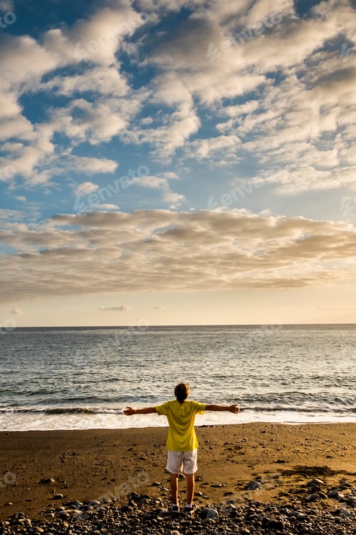 Preview: Colorful sunset at the beach and young man standing and enjoying the beauty of nature and ocean