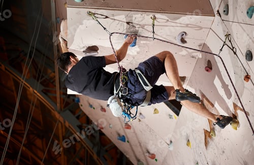 Preview: man pushing himself higher to reach the top of artificial climbing wall in bouldering gym