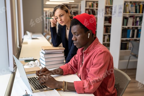 Preview: College tutor woman assists puzzled student African American guy in solve task at laptop in library.