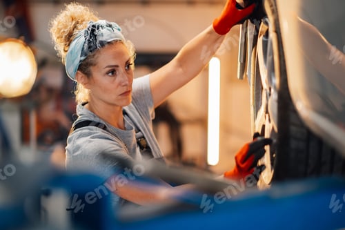 Preview: Portrait of female auto mechanic fixing and changing car tyre at shop.