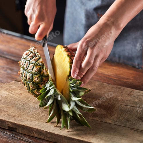 Preview: The girl's hand with a knife cuts a tropical fruit pineapple on a board on a wooden brown table
