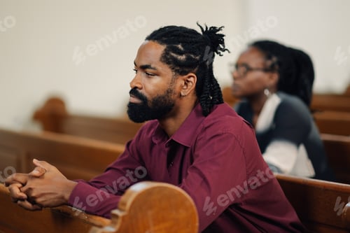 Preview: Young man praying in church with people in background