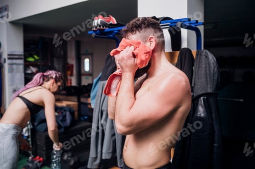 Preview: Bare chested young man training, drying face with towel in gym