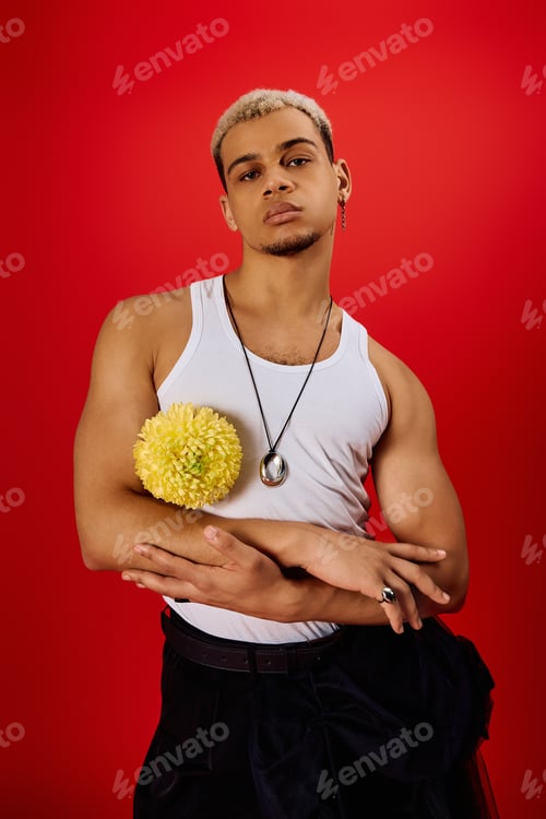 Preview: Stylish young man in trendy tank top poses gracefully with a flower in a vibrant studio