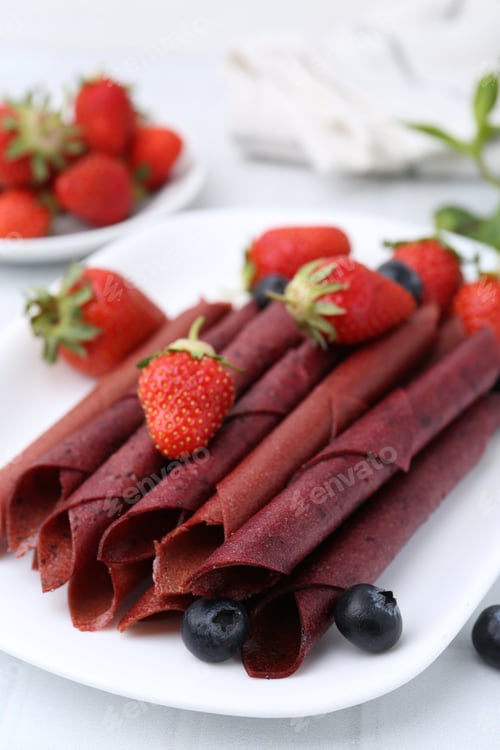 Preview: Tasty fruit leather rolls, strawberries and blueberries on white table, closeup