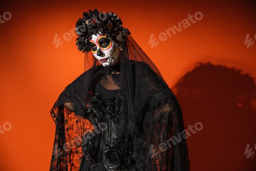 Preview: woman in mexican day of dead makeup and costume with black lace veil posing on orange background