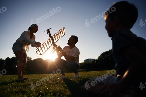 Preview: Mother, father and son are on field with toy plane, dark colors, dawn