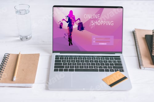 Preview: notebooks and laptop with shopping website on screen and credit card on wooden desk