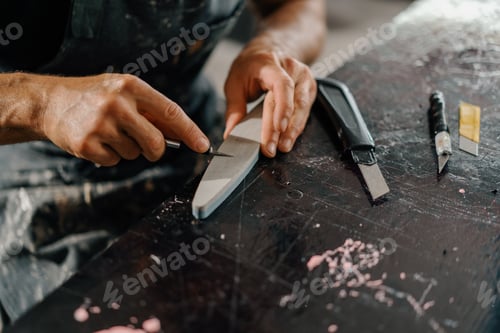 Preview: Close-up: artisan sculptor artist sharpening a blade on a sharpener in a workshop
