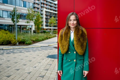 Preview: portrait of a woman at the red wall of a modern office building on a cool autumn day