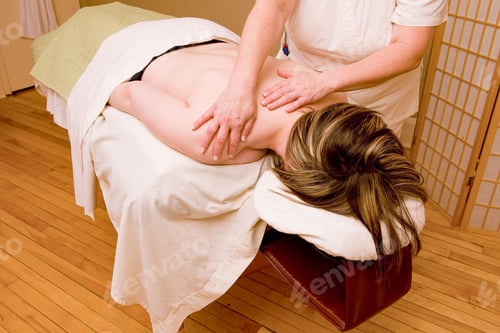Preview: Woman lying on a massage table with small rocks and being massaged