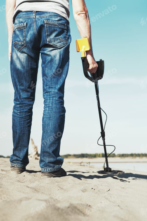 Preview: Man with metal detector walks along the sandy river bank. Search treasures and metal for recycling