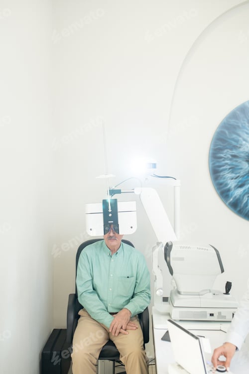 Preview: Senior male patient looking through lens during medical check-up of his eyesight