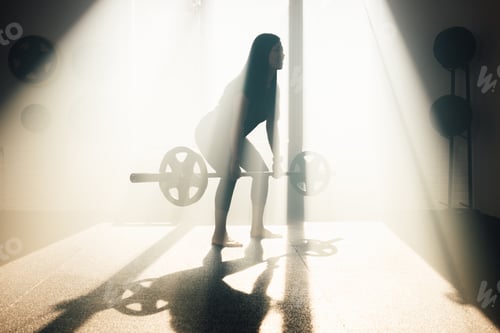 Preview: Young woman doing weightlifting exercises in gym