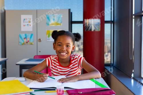 Preview: Happy african american schoolgirl sitting at desk and learning in classroom at elementary school