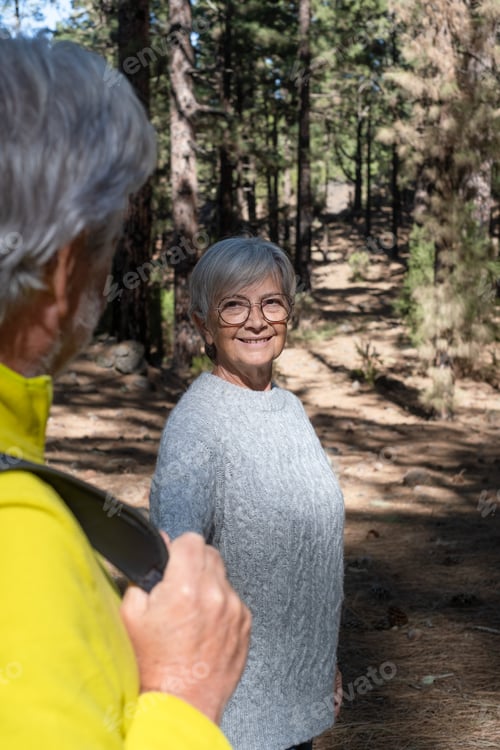Preview: Attractive senior woman looking at his husband walking in the forest holding his hand