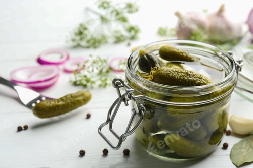 Preview: Glass jar of pickled cucumbers on white wooden table. Space for text