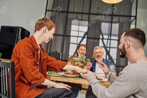 Preview: gay man holding wedding ring while making marriage proposal to boyfriend during family supper at