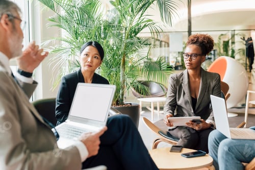 Preview: Three professionals engaged in a serious business discussion in a modern office lobby.