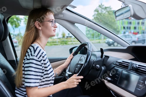 Preview: Teenage girl driver in glasses sitting behind wheel of car