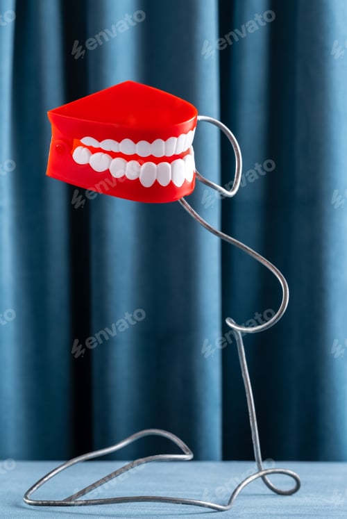 Preview: A model of a human jaw biting a metal wire, still life on a background of blue curtains.
