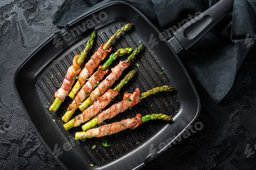 Preview: Fried bacon wrapped asparagus in a grill skillet. Black background. Top view