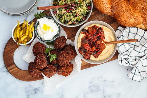 Preview: Traditional Shabbat table: challah bread, falafel, quinoa salad, hummus on a wooden board.