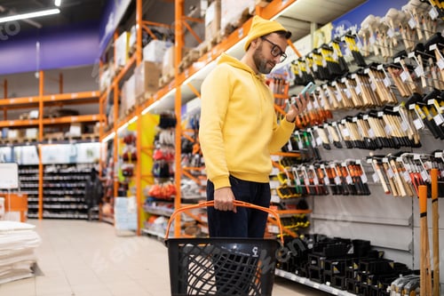 Preview: a young man in a hardware store next to a rack with hammers and axes looks at the smartphone screen