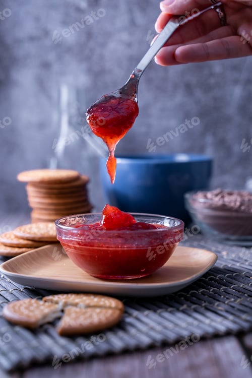 Preview: Vertical shot of a hand holding a spoon of strawberry jam