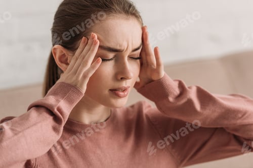 Preview: young woman holding hands near head while suffering from migraine with closed eyes