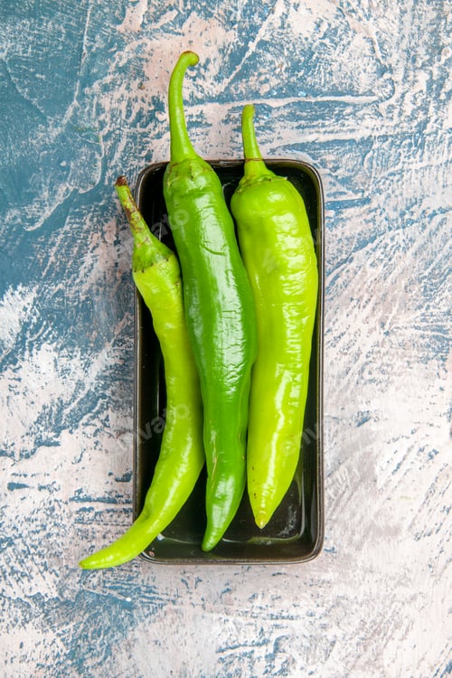 Preview: top view green hot peppers on black plate on blue-white background