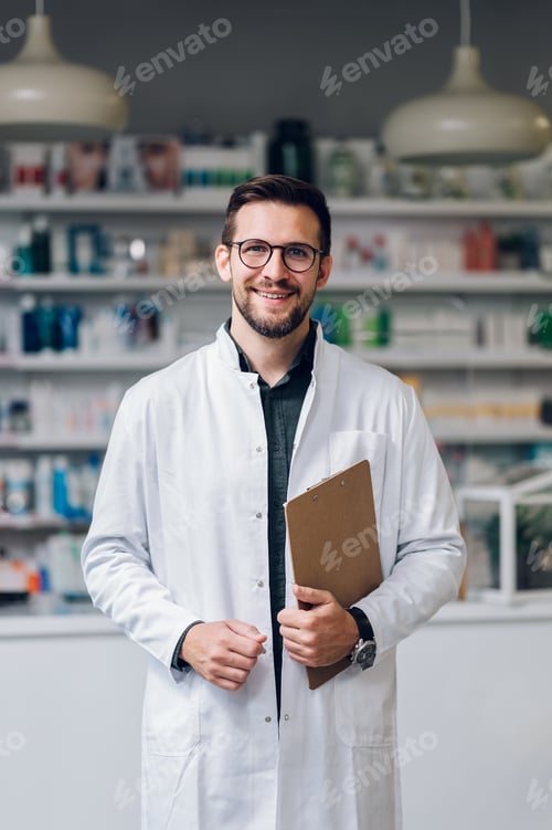 Preview: Portrait of a friendly happy pharmacist standing in a drug store with a clipboard in his hands