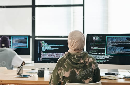 Preview: Rear view of young Muslim woman sitting in front of computer screens