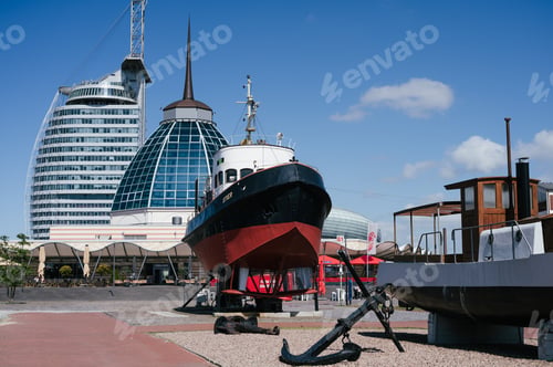 Preview: Impressive vessel is docked at a pier in front of a modern cityscape.