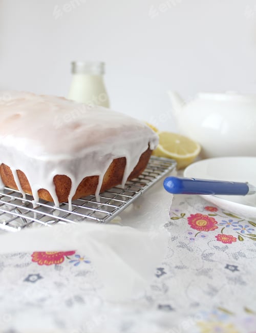 Preview: Freshly baked iced lemon cake on a cooling rack with tea and plate